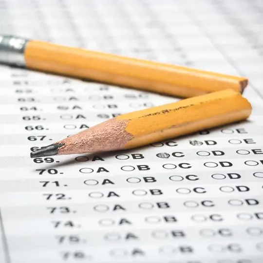 A close-up view of a standardized test answer sheet with several bubbles marked. A broken yellow pencil is positioned near the answer sheet, which has numbers 67 through 72 visible, with various answer choices labeled A, B, C, and D.